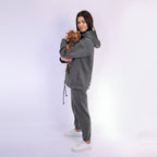 Woman wearing a gray tracksuit holding a small dog on a white background