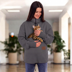 Women wearing a gray sweatshirt with a cat in the pouch on a blurred indoor background