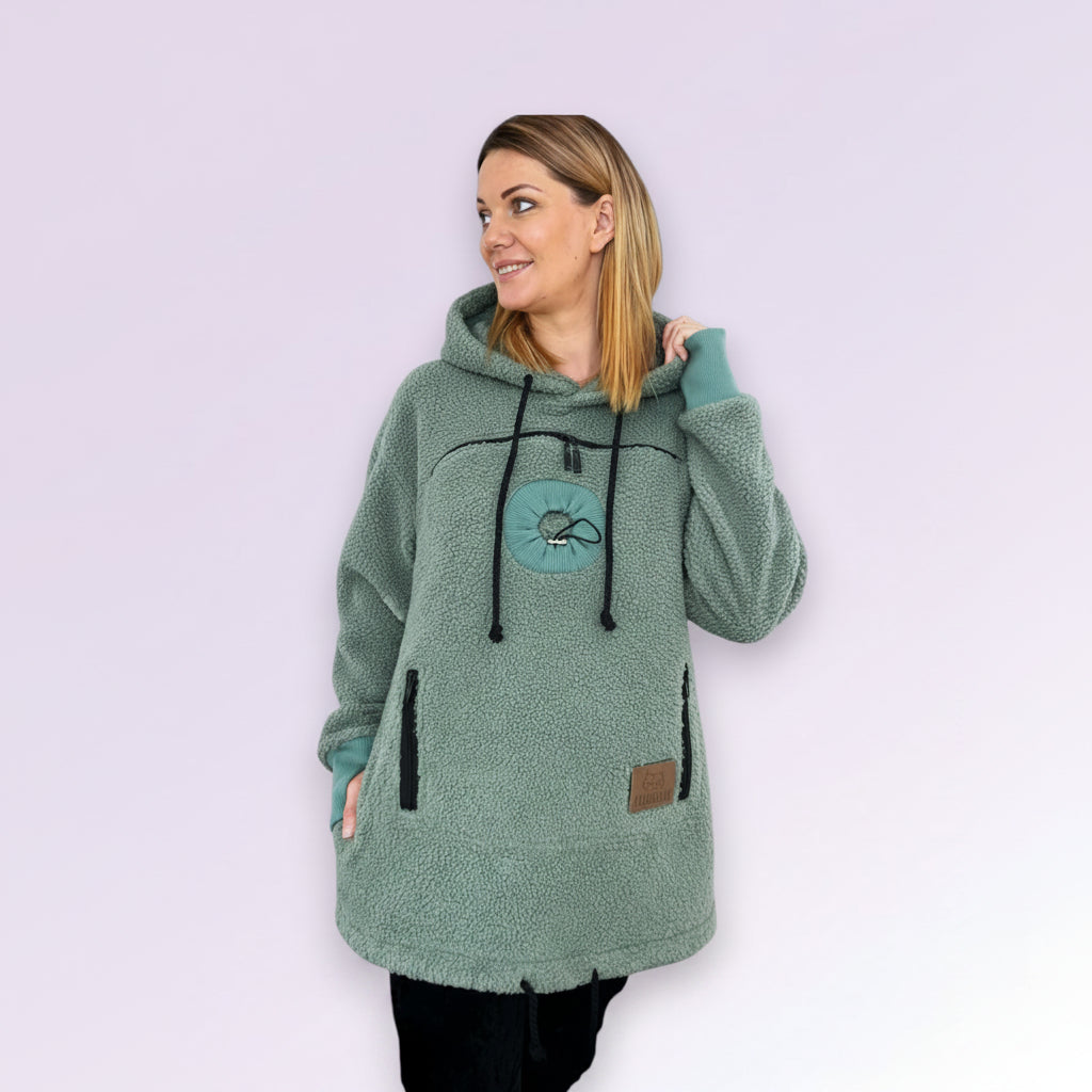 Woman wearing a green fleece hoodie with a logo on a light purple background