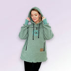 Person wearing a green fleece hoodie with a brand logo on a light purple background