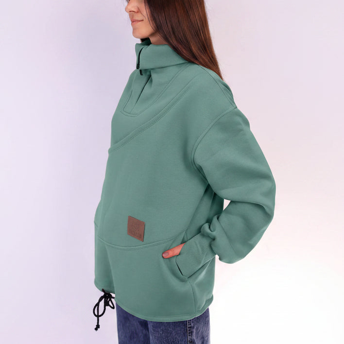 Person wearing a green pullover with a brown patch on a light purple background