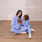 Two people in matching light blue outfits sitting on the floor with a small dog.