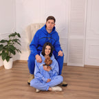 Two people in matching blue and light blue onesies sitting on the floor with a small dog.