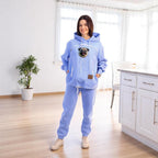 Person wearing a light blue hoodie and pants with a pug in a kitchen.