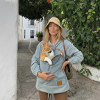 Woman wearing a light blue denim hoodie with a cat in the front pouch on a European street