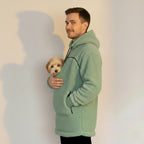 Man wearing a light green fleece jacket holding a small dog against a plain background