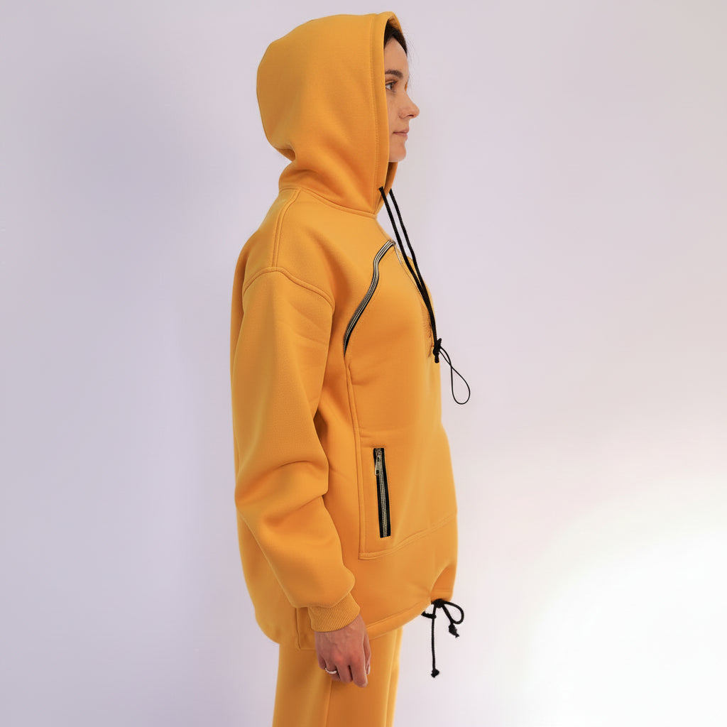 Person wearing a mustard hoodie with zippers on a white background