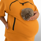 Person wearing an orange garment with a pocket holding a gray cat.