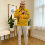 Man in orange boucle hoodie holding a cat in a room with wooden floor and white walls.