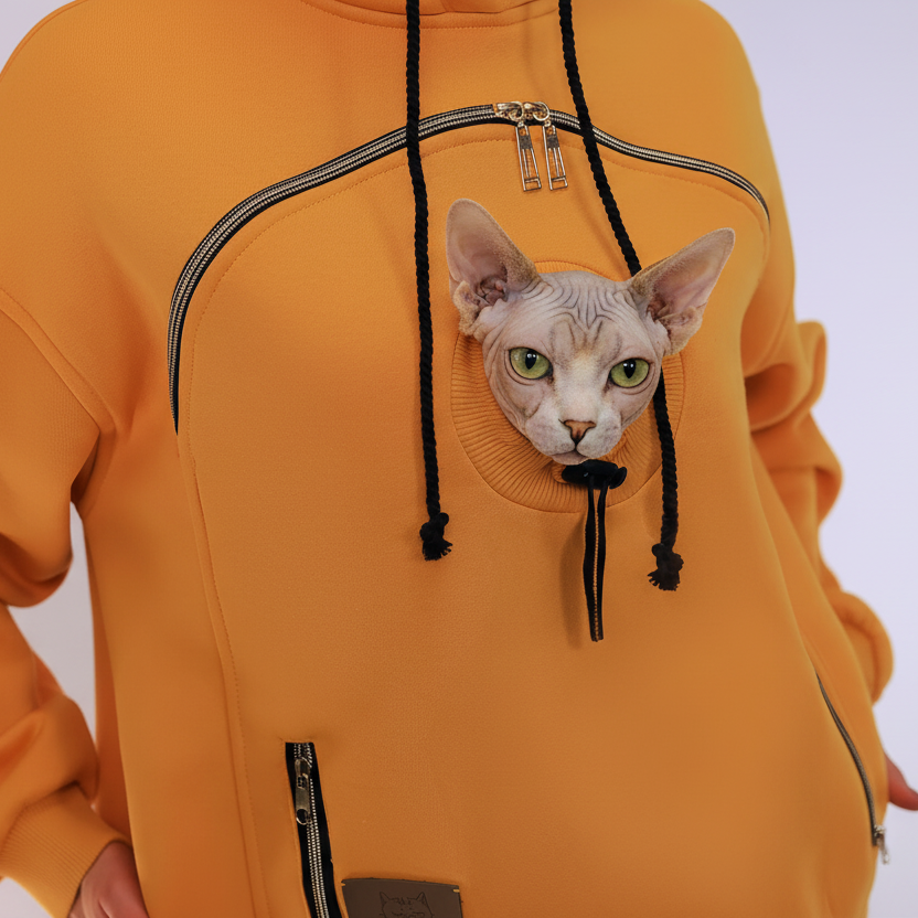 Person wearing a orange hoodie with a small hairless cat peeking out from inside the hood.