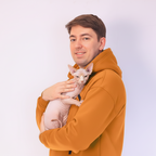 Man in an orange hoodie holding a white hairless cat against a light background