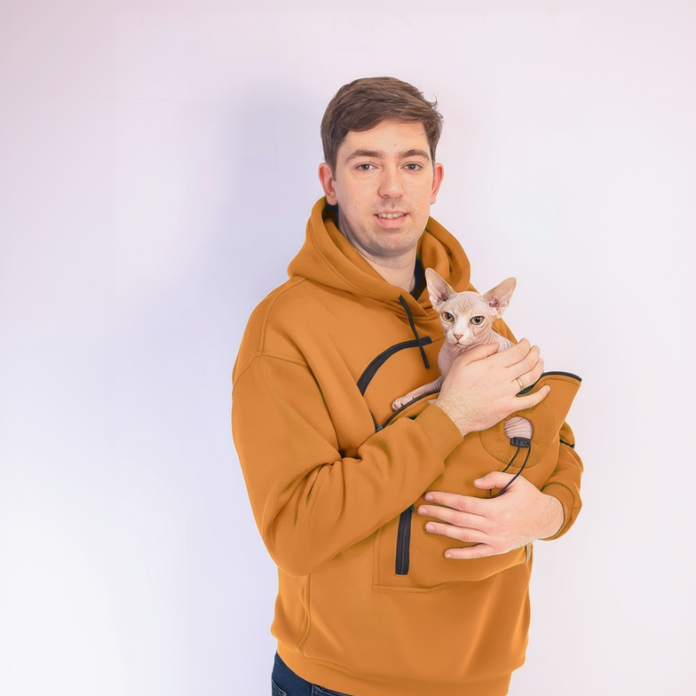 Man wearing an orange hoodie holding a small white cat against a plain background