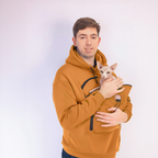Man wearing an orange hoodie holding a small white cat against a plain background