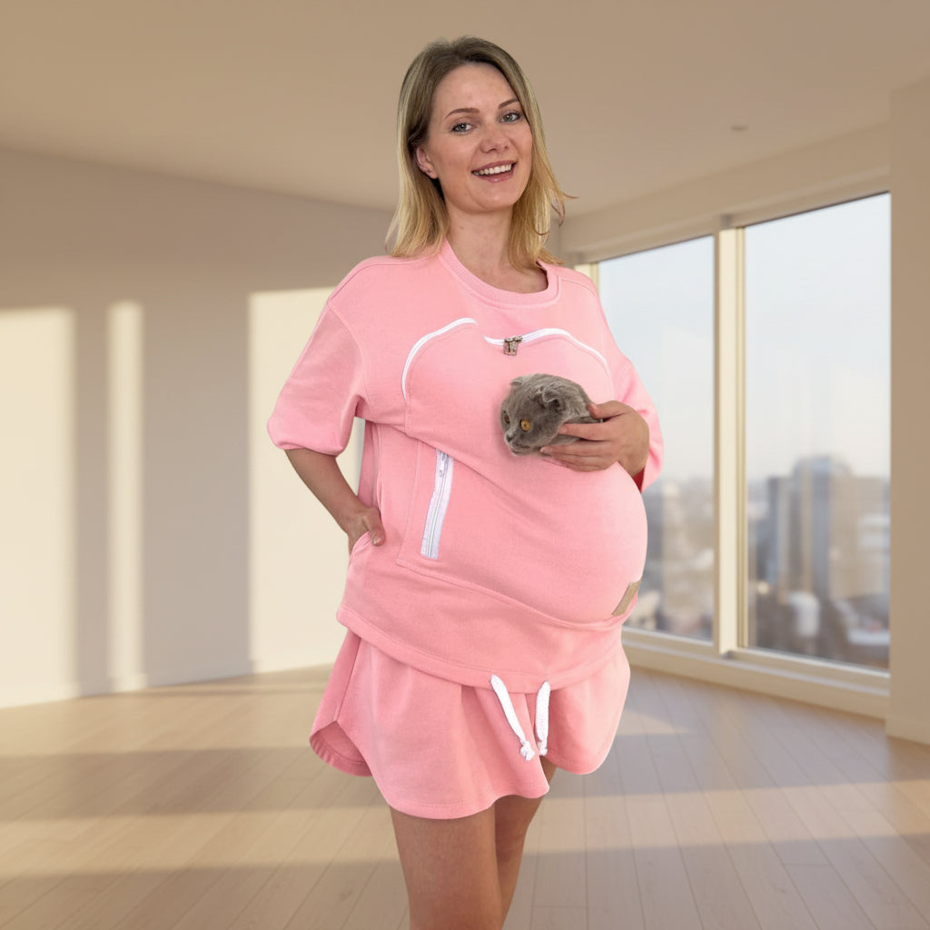 Woman wearing a pink outfit with a pouch, holding a small animal against a white background