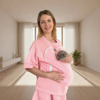 Woman wearing a pink carrier holding a cat in a bright room.
