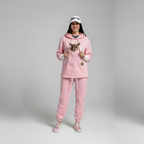 Person wearing a pink tracksuit with a small dog in a hoodie, on a gray background
