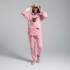 Person wearing a pink tracksuit with a small dog on a gray background