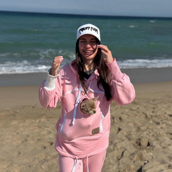 Person in pink hoodie with dog in pocket on beach