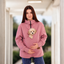 Women wearing a pink sweatshirt with a dog in pouch, standing indoors.
