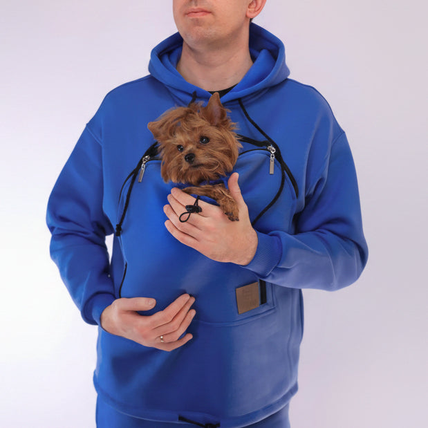 Men wearing a royal blue hoodie with a pocket holding a small dog on a white background