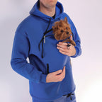 Men wearing a royal blue hoodie with a front pocket holding a small brown dog.