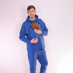 Man wearing a royal blue tracksuit holding a small dog on a white background