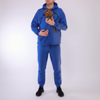 Person wearing a royal blue hoodie with a pocket holding a small dog on a white background