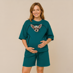 Woman wearing a teal outfit with a heart design featuring a dog, standing against a beige background.
