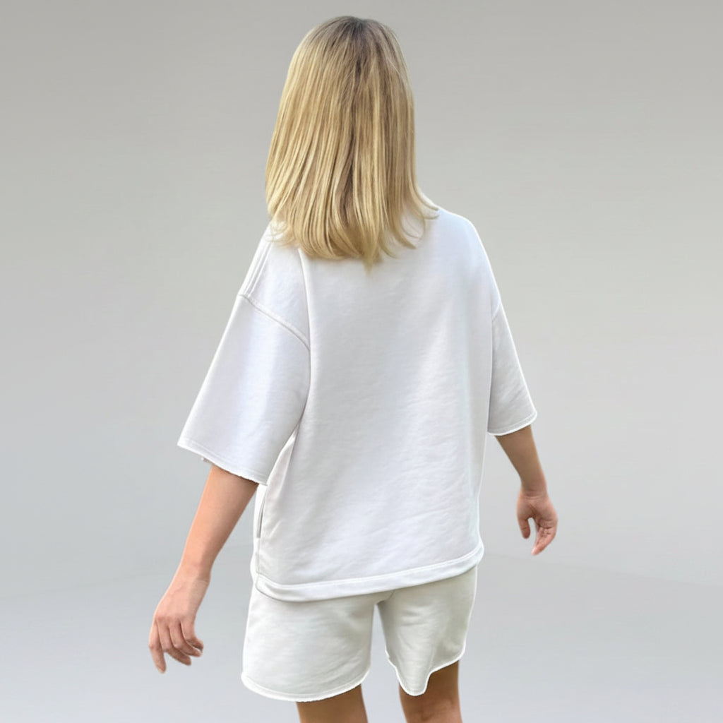 Person wearing a white oversized t-shirt and shorts set on a plain background