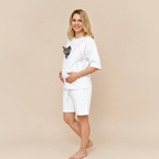 Woman wearing a white t-shirt with a cat in the pocket and shorts, standing against a beige background