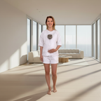 Woman in a white outfit standing in a modern, sunlit room with large windows.