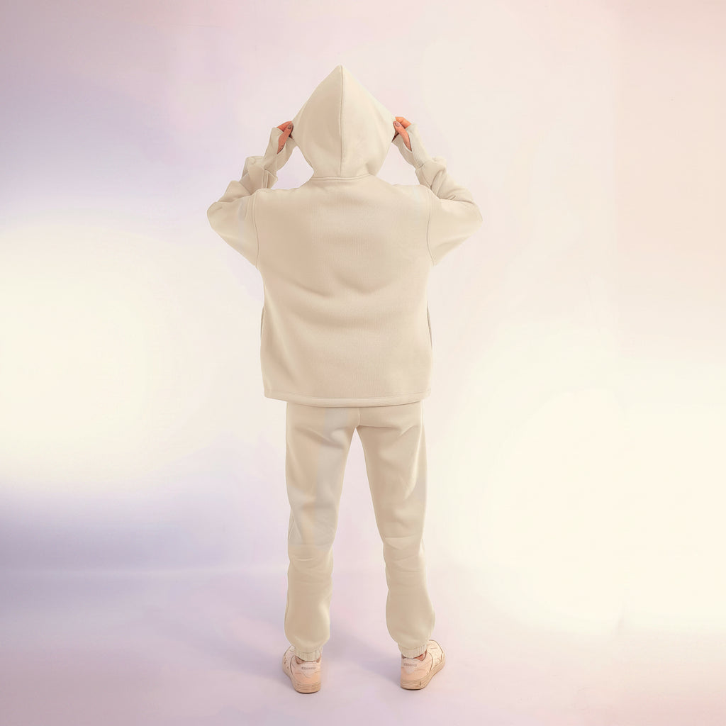 Person wearing a white hoodie and pants set on a light pink background