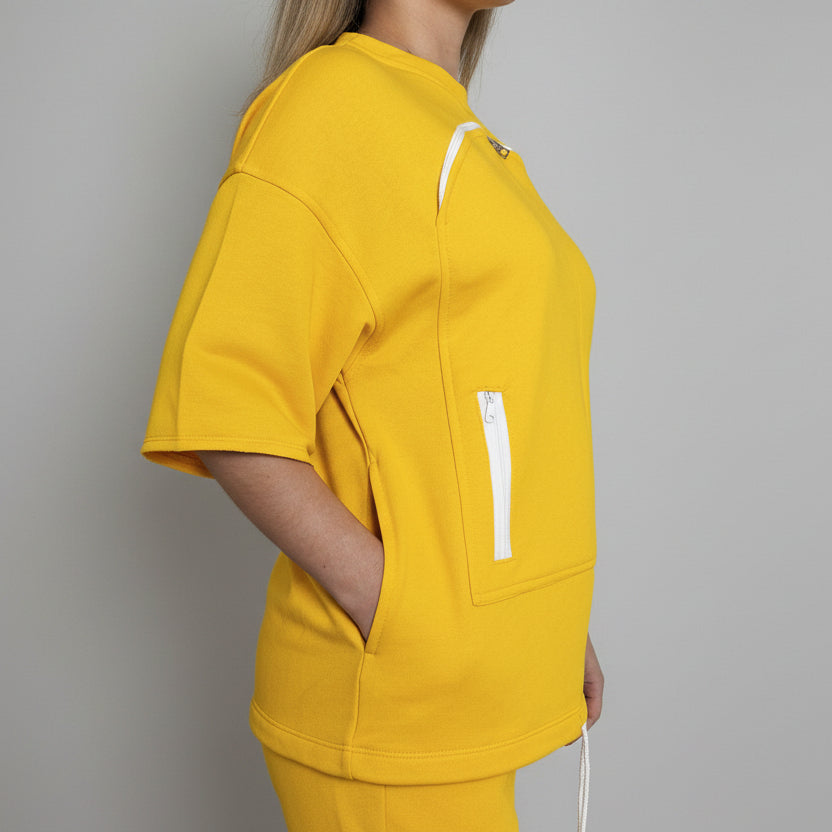 Person wearing a yellow outfit with a white zipper detail indoors.
