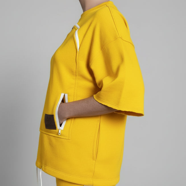 Person wearing a yellow outfit with a white zip in a room.