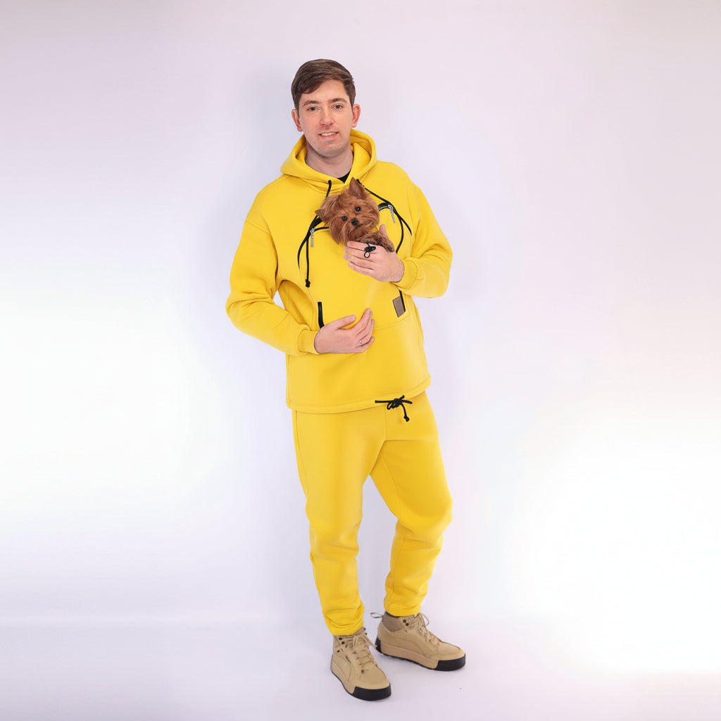 Person wearing a yellow hoodie and matching pants holding a small dog on a white background Main image