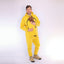 Person wearing a yellow hoodie and matching pants holding a small dog on a white background