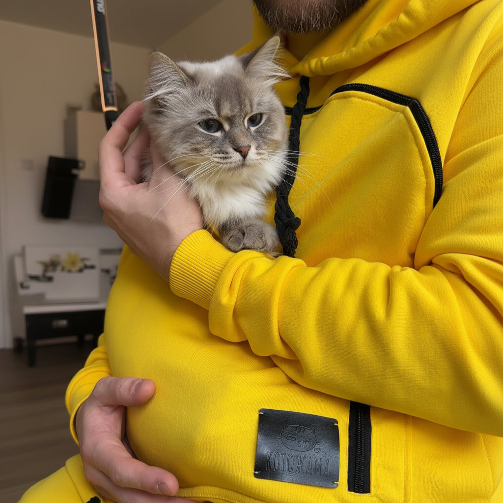 Person wearing a yellow hoodie holding a gray kitten